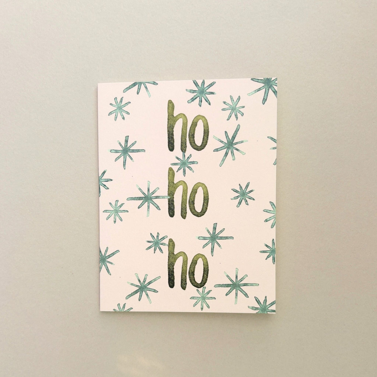 Ho Ho Ho Christmas greeting card by Merrier in pink: stacked 'ho ho ho' lettering surrounded by teal snowflakes